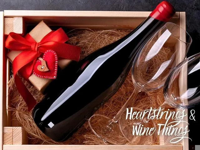 Wooden gift box containing a wine bottle, two wine glasses, and a small wrapped gift tied with a red ribbon and heart-shaped tag, with the title "Heartstrings & Wine Things."