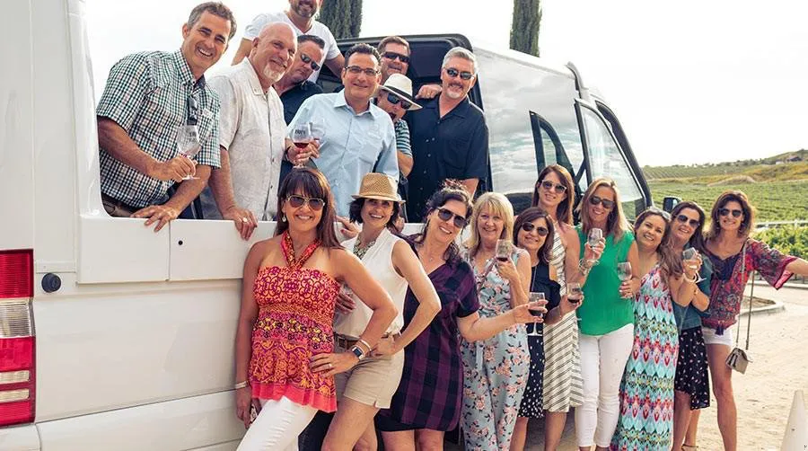 Friends pose infront of a Mercedes convertible shuttle with wine glasses